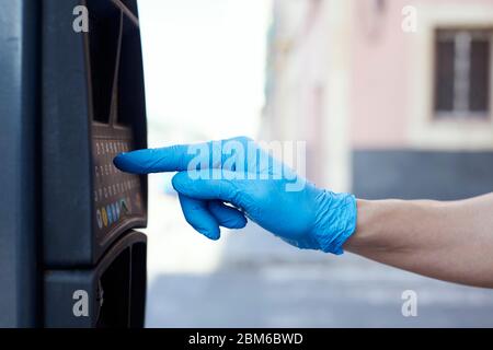 primo piano di un giovane, indossando guanti blu in lattice, utilizzando un parchimetro elettronico sulla strada Foto Stock