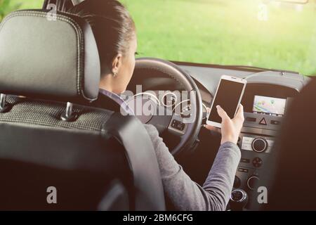 Femmina giovane conducente utilizzando il touch screen smartphone e la navigazione gps in un'auto. Foto Stock