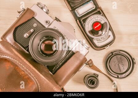 Vintage vecchia foto-telecamera in custodia in pelle con esposimetro, cassetta a nastro e copriobiettivo su sfondo di legno. Foto Stock