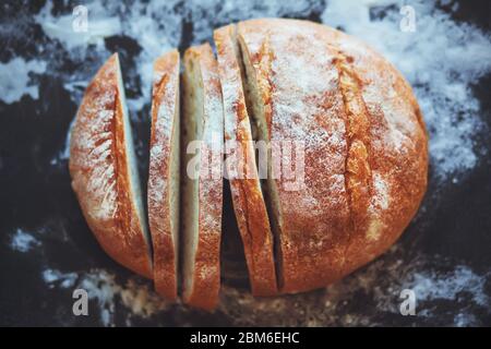 Vista dall'alto del pane fresco a fette di frumento adagiato su uno sfondo nero macchiato di farina. Torta fatta in casa. Foto Stock