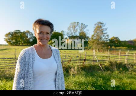 Felice donna matura bella in piedi in pianura erbosa pacifica con la natura Foto Stock