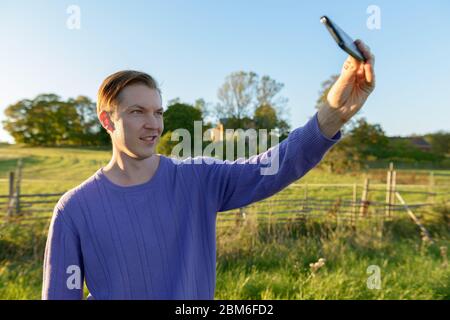 Felice giovane bell'uomo che prende selfie in tranquilla pianura erbosa con la natura Foto Stock