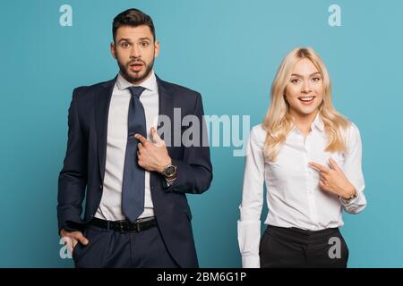 sorpreso uomo d'affari e donna d'affari puntando con le dita a se stessi su sfondo blu Foto Stock