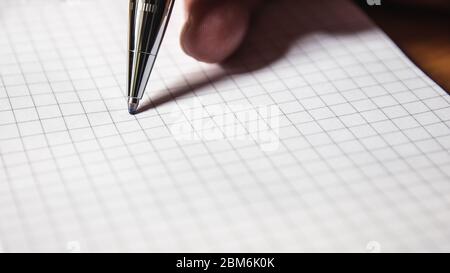 Un uomo scrive in un notebook aperto in una gabbia con una penna a sfera automatica in plastica primo piano. Foto Stock