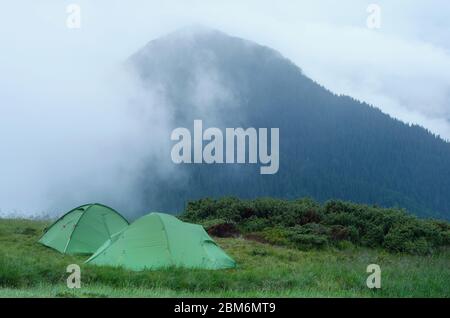 Paesaggio di montagna con campeggio. Due verdi tende turistiche. Nebbia serale. Carpazi, Ucraina Foto Stock