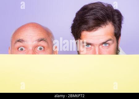Due uomini sorpresi che tengono carta vuota. Presentazione. CopySpace. Vecchio e giovane, padre figlio. Uomo anziano sorpreso e uomo divertente che tiene carta vuota. COP Foto Stock