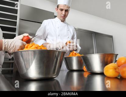 chef di pasticceria al lavoro in cucina professionale, prepara marmellata di albicocche per la torta o per i croissant, su piano di lavoro in acciaio inox Foto Stock