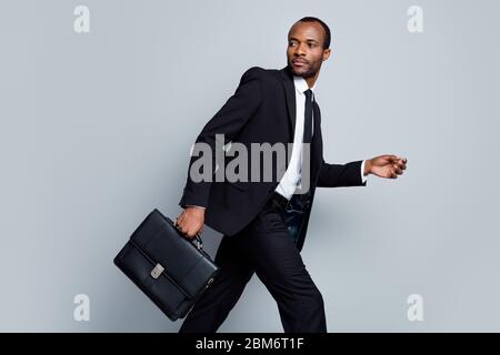 Profilo foto laterale di occupato maschile afro agente broker americano uomo andare a piedi tenere borsa fretta per business partnership meeting indossare nero blazer Foto Stock