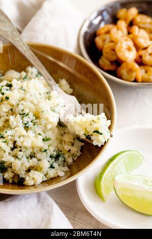 Riso al cavolfiore a basso contenuto di carb o couscous con coriandolo tritato e lime in un primo piano ciotola marrone.salutare contorno vegetariano Foto Stock