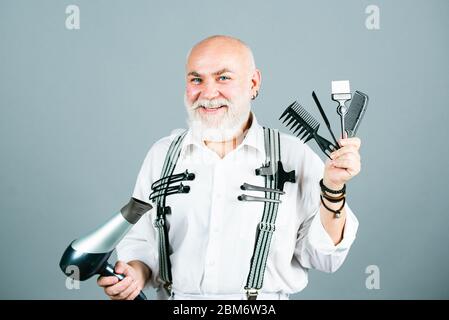 Parrucchiere senior. Uomo barbuto, anziano barbuto nel salone di bellezza. Ritratto di elegante parrucchiere uomo con barba bianca. Parrucchiere Barbiere che tiene i capelli Foto Stock