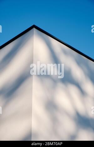 Un'architettura astratta di due pareti e un angolo di una casa moderna con intonaco bianco contro il cielo azzurro. Visto in Germania nel mese di marzo. Foto Stock