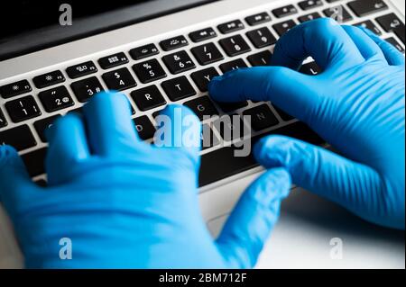 Lavorare con guanti di protezione su un computer. Concetto di prevenzione del coronavirus. Lavoro sicuro in ufficio con notebook. Foto Stock