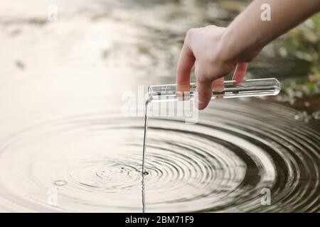 una mano di uno specialista aspira l'acqua in un pallone da un fiume per ulteriori ricerche in laboratorio. controlla il livello di inquinamento idrico. concentrazione selettiva Foto Stock