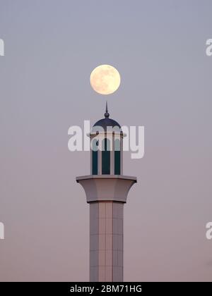 Una luna piena sorge da dietro un minareto della moschea Baitul Futah a Morden, nel sud-ovest di Londra, il 6 maggio. Era l'ultima superluna del 2020. Foto Stock