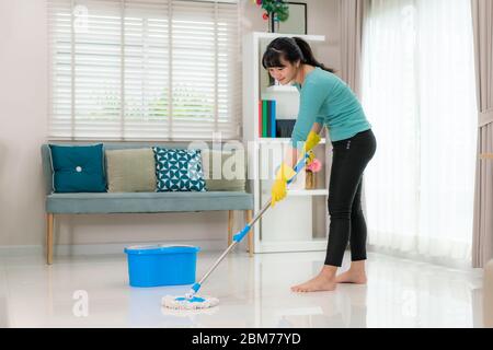 Attraente giovane donna asiatica che pulisce il pavimento delle mattonelle al soggiorno mentre fa la pulizia a casa durante il soggiorno a casa usando il tempo libero circa la loro h quotidiana Foto Stock
