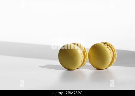 Modello astratto con macaroni gialli o macaron su sfondo bianco con ombre. Ripetizione senza giunture. Delizioso e salutare dessert francese. Mini creativo Foto Stock