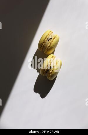 Modello astratto con macaroni gialli o macaron su sfondo bianco con ombre. Ripetizione senza giunture. Delizioso e salutare dessert francese. Mini creativo Foto Stock