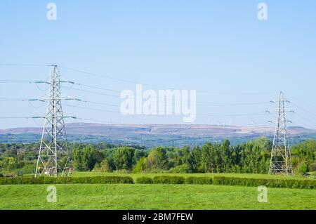 Piloni elettrici in Inghilterra con parco eolico in background - campi inglese piloni distribuzione di campo rete energia alta tensione torre di trasmissione Foto Stock