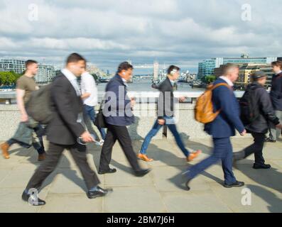 Lavoratori della città dal quartiere finanziario di Londra all'ora di punta camminando sopra il London Bridge alla fine della giornata lavorativa, con Tower Bridge sullo sfondo Foto Stock