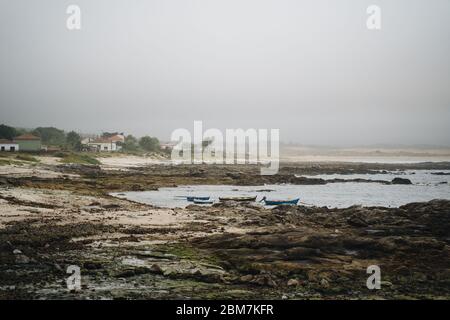 Oceano Atlantico mare a Corrubedo con barche e costa rocciosa nel nord della Spagna con clima fogy Foto Stock