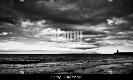 immagine in bianco e nero mentre la marea sta facendo girare le onde delicatamente rompendo. L'orizzonte è pieno di spettacolari nuvole scure, costa scozzese, Scozia Foto Stock