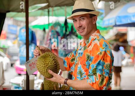 Felice giovane bel turista uomo che acquista durian al mercato di strada Foto Stock