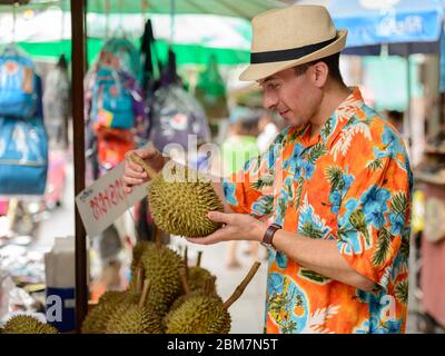 Felice giovane bel turista uomo che acquista durian al mercato di strada Foto Stock