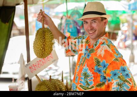 Felice giovane bel turista uomo che acquista durian al mercato di strada Foto Stock