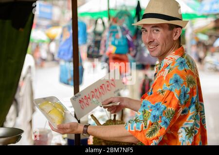 Felice giovane bel turista uomo che acquista durian al mercato di strada Foto Stock