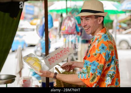 Felice giovane bel turista uomo che acquista durian al mercato di strada Foto Stock