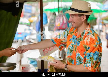 Felice giovane bel turista uomo che acquista durian al mercato di strada Foto Stock