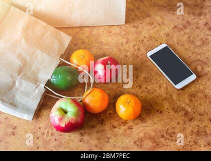 Sacchetti di carta, verdure fresche e frutta accanto al telefono cellulare sul tavolo da cucina. Acquisto online e consegna senza contatto. Foto Stock