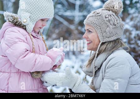 Il bambino costruisce un pupazzo di neve in inverno con una madre che ride Foto Stock