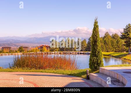 Bella vista del paesaggio autunnale del lago, pini, chalet in legno e montagne sullo sfondo vicino Bansko, Bulgaria Foto Stock