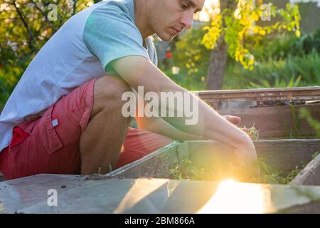 Maschio serio in vestiti casual piantando pomodori nella serra fatta a mano a casa Foto Stock