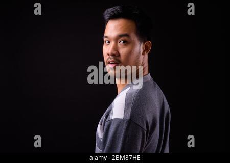 Vista posteriore del giovane asiatico guardando la macchina fotografica Foto Stock