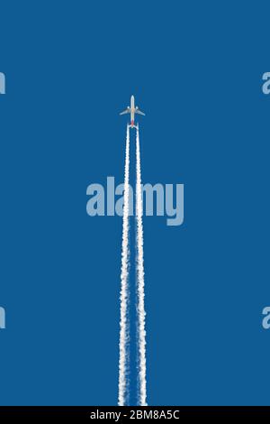 Contrasti (cirrus homogenitus) di un grande jet piano bianco alto nel cielo blu Foto Stock