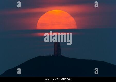 Glastonbury, Somerset, Regno Unito. 7 maggio 2020. Meteo Regno Unito. La luna piena si erge da dietro Glastonbury Tor nel Somerset ma è parzialmente oscurata dalla nuvola che la rende arancione scuro. Questo mese luna è chiamato il fiore luna ed è l'ultima superluna dell'anno. Credito immagine: Graham Hunt/Alamy Live News Foto Stock