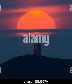 Glastonbury, Somerset, Regno Unito. 7 maggio 2020. Meteo Regno Unito. La luna piena si erge da dietro Glastonbury Tor nel Somerset ma è parzialmente oscurata dalla nuvola che la rende arancione scuro. Questo mese luna è chiamato il fiore luna ed è l'ultima superluna dell'anno. Credito immagine: Graham Hunt/Alamy Live News Foto Stock