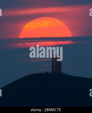 Glastonbury, Somerset, Regno Unito. 7 maggio 2020. Meteo Regno Unito. La luna piena si erge da dietro Glastonbury Tor nel Somerset ma è parzialmente oscurata dalla nuvola che la rende arancione scuro. Questo mese luna è chiamato il fiore luna ed è l'ultima superluna dell'anno. Credito immagine: Graham Hunt/Alamy Live News Foto Stock