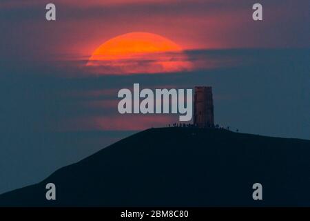 Glastonbury, Somerset, Regno Unito. 7 maggio 2020. Meteo Regno Unito. La luna piena si erge da dietro Glastonbury Tor nel Somerset ma è parzialmente oscurata dalla nuvola che la rende arancione scuro. Questo mese luna è chiamato il fiore luna ed è l'ultima superluna dell'anno. Credito immagine: Graham Hunt/Alamy Live News Foto Stock