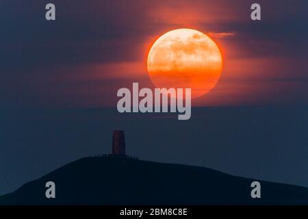 Glastonbury, Somerset, Regno Unito. 7 maggio 2020. Meteo Regno Unito. La luna piena si erge da dietro Glastonbury Tor nel Somerset ma è parzialmente oscurata dalla nuvola che la rende arancione scuro. Questo mese luna è chiamato il fiore luna ed è l'ultima superluna dell'anno. Credito immagine: Graham Hunt/Alamy Live News Foto Stock