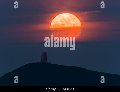 Glastonbury, Somerset, Regno Unito. 7 maggio 2020. Meteo Regno Unito. La luna piena si erge da dietro Glastonbury Tor nel Somerset ma è parzialmente oscurata dalla nuvola che la rende arancione scuro. Questo mese luna è chiamato il fiore luna ed è l'ultima superluna dell'anno. Credito immagine: Graham Hunt/Alamy Live News Foto Stock