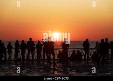 Silhouette di persone contro il tramonto sul ponte di una nave da crociera. Oceano calmo e cielo arancione chiaro in serata. Vacanze di crociera sfondo Foto Stock