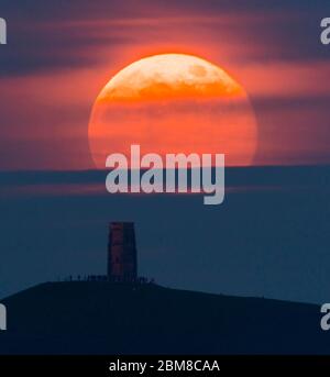 Glastonbury, Somerset, Regno Unito. 7 maggio 2020. Meteo Regno Unito. La luna piena si erge da dietro Glastonbury Tor nel Somerset ma è parzialmente oscurata dalla nuvola che la rende arancione scuro. Questo mese luna è chiamato il fiore luna ed è l'ultima superluna dell'anno. Credito immagine: Graham Hunt/Alamy Live News Foto Stock