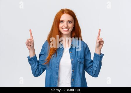 Girovita ritratto sicuro felice, seducente donna rossa in denim camicia, punta le dita su, sorridente in senso lato, raccomandare l'assistenza aziendale, mostrare Foto Stock