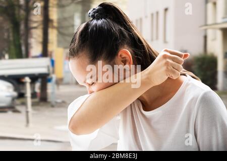 Influenza Sick Donna starnutito in Elbow all'aperto Foto Stock