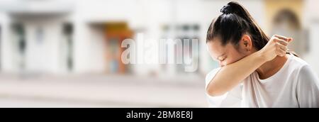 Influenza Sick Donna starnutito in Elbow all'aperto Foto Stock