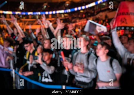 Sfondo sfocato di un evento di eSport - un sacco di fan su una tribuna all'arena del torneo con le mani sollevate. Rallegrarsi per la loro squadra preferita. Foto Stock