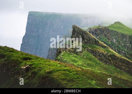 Vista foggy delle montagne meravigliose dell'isola di Mykines con turista sul punto panoramico alto. Isole Faroe, Danimarca. Fotografia di paesaggio Foto Stock